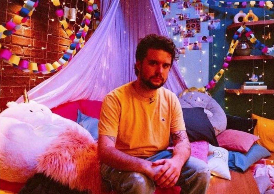 specer sitting with his hands together on a colorful set with fairy lights, a canopy, and lots of pillows
